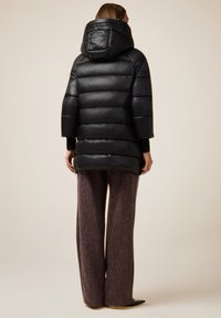 Giacca a vento nera con cappuccio, caratterizzata da un design trapuntato e maniche larghe. Il materiale è liscio con una finitura lucida. Indossata sopra pantaloni marroni con texture.