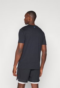 Sort T-shirt med korte ærmer lavet af bomuld, med rund hals og et lille blåt logo på ryggen, parret med sorte sportsshorts.