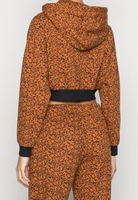 Hoodie corto arancione con motivo animalier nero, dotato di cappuccio e polsini neri, realizzato in morbido tessuto strutturato.