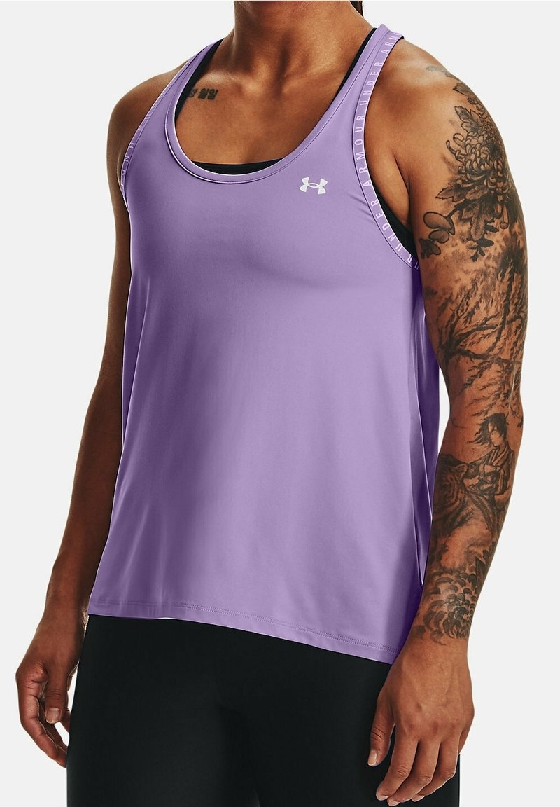 Personne portant un haut de sport sans manches violet Under Armour, montrant des tatouages floraux et figuratifs détaillés sur le bras droit.