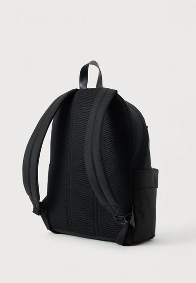 Sac à dos noir avec bretelles rembourrées, panneau arrière en mesh respirant et poignée de transport supérieure sur un fond clair uni.