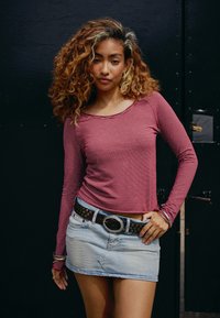 Long-sleeve maroon-striped shirt with a round neckline paired with a light denim mini skirt. Black belt with metallic studs at the waist.