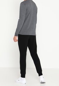 Graues Langarmshirt kombiniert mit schwarzen Jogginghosen. Das Outfit zeichnet sich durch gerippte Bündchen, eine lässige Passform aus und wird durch weiße Sneakers ergänzt.