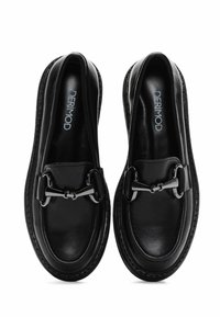 Mocasines de cuero negro con un acabado brillante, que presentan una hebilla metálica decorativa y costuras en contraste a lo largo de la suela. Perfil plano.