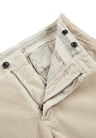 Beige corduroy broek met een ritssluiting aan de voorkant, twee zwarte knopen en een gestructureerde stof. De binnenkant is gevoerd met een visgraatpatroon.