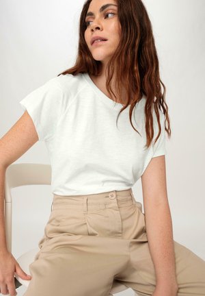 Lichtgrijze, kortschild t-shirt met een relaxte pasvorm, gecombineerd met beige hoge taille broek met een knoopdetail. Zachte stoftextuur.