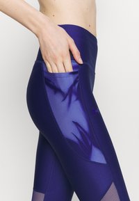 Fioletowe legginsy sportowe z boczną kieszenią, gładką fakturą i siateczkowym panelem zapewniającym przewiewność i styl.