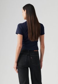 T-shirt ajustada azul-marinho de mangas curtas, combinada com jeans pretos de cintura alta, apresentando um logótipo Levi's e costura distinta no bolso traseiro.