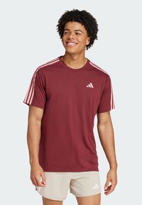 Camiseta de manga corta color granate con un diseño rosa de tres rayas en los hombros y un pequeño logo blanco en el pecho. Tejido suave, ajuste regular.