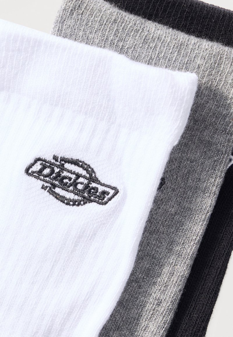 Three folded socks in white, light gray, and black, with a visible black embroidered logo on the white sock.