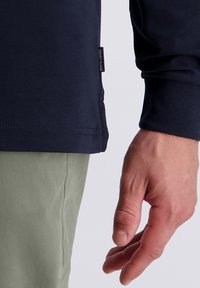 Marineblauwe longsleeve shirt met een ronde hals en gebreide manchetten, gecombineerd met lichtgroene broek. Beschikt over een label met de merknaam aan de zoom.