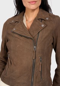 Hnědá koženka s předním zipem a bočními kapsami, se stříbrnými detaily a mírně texturovaným povrchem.