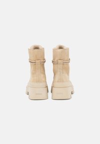 Bottines en suède beige avec une doublure douce, bout rond et semelle en caoutchouc épaisse. Chaque botte dispose d'une sangle décorative près de la cheville.