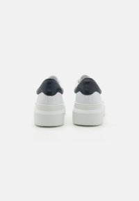 Hvite sneakers med en teksturert hvit såle, med en blank marineblå hælakkent og et glatt overdesign.