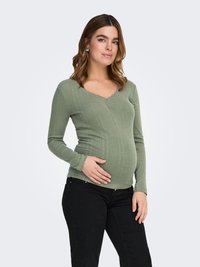 Barsel top i ribbet, blødt grønt stof med V-udskæring og bølget kant. Kombineret med sorte bukser, sidder tæt over maven.
