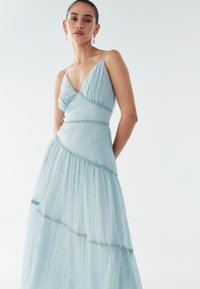 Světlomodré maxi šaty s tenkými ramínky, s výstřihem do V, vrstveným designem a texturovanou látkou zvýrazněnou jemným prošíváním.