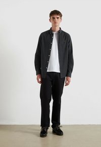 Ciemnoszara koszula zapinana na guziki z delikatną teksturą, nałożona na gładki biały t-shirt. Połączona z czarnymi spodniami i ciemnymi butami.