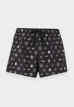 Shorts de bain noirs avec des motifs blancs de soleil, signes de paix, couronnes, lunettes de soleil, et logos "Moschino Swim" partout, avec une ceinture à cordon noire.