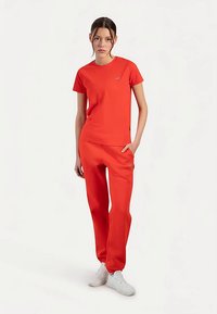 Rood T-shirt met korte mouwen, gecombineerd met bijpassende broek, beide gemaakt van gladde stof. Voorzien van een klein logo op het shirt, een slim-fit pasvorm en zijzakken.