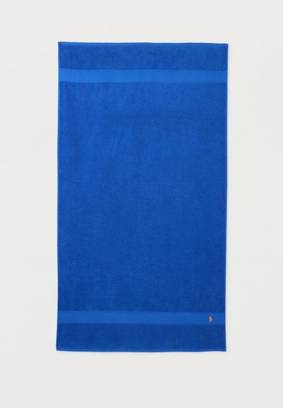 Στερεή μπλε ορθογώνια πετσέτα με δύο σκουρότερες μπλε ρίγες κοντά στις άκρες και μικρό πορτοκαλί λογότυπο στην κάτω δεξιά γωνία.