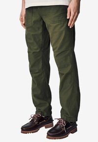 Pantalons cargo vert olive avec une coupe décontractée, dotés de poches latérales et d'un tissu résistant. Associés à des chaussures en cuir marron à lacets.