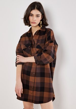 Brown and black plaid shirt dress with long sleeves, button front, and chest pockets. Soft fabric with a relaxed fit, mid-thigh length.