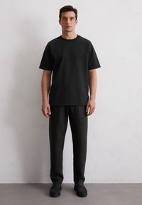 Zwarte katoenen t-shirt met een ronde hals, gecombineerd met donkergrijze linnen broek en zwarte instappers, gepresenteerd tegen een neutrale achtergrond.