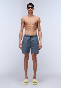 Gray swim shorts with a drawstring waist, contrasting black accents, paired with lime green slip-on shoes and dark sunglasses.