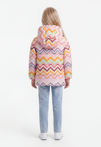 Enfant de dos portant une doudoune à capuche colorée avec un motif en zigzag, un jean bleu clair et des baskets blanches sur fond blanc.
