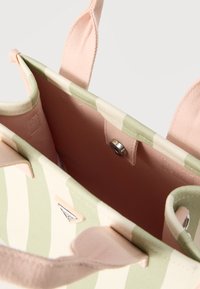 Τσάντα ώμου από καμβά με πράσινες και λευκές ρίγες, ροζ εσωτερικό και λαβές, και μεταλλικό κούμπωμα στο επάνω κέντρο.