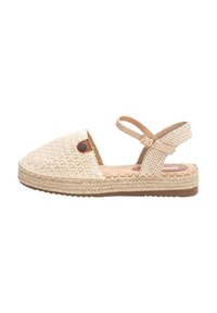 Sandalia de espadrille trenzada en beige con suela plana, correa ajustable en el tobillo y un acabado texturizado. Presenta un acento de logo redondo en el costado.