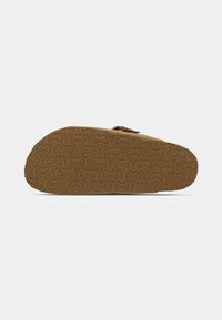 Sole of tan sandal with textured interlocking circular pattern and adjustable strap buckle visible on top edge.