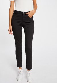 Zwarte slim fit jeans met een gladde textuur, een knoopsluiting en zijzakken. Gecombineerd met witte sneakers voor een casual look.