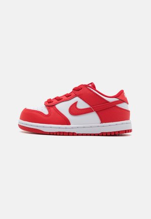Low-Top Nike Sneaker aus weißem und rotem Leder mit roten Schnürsenkeln und roter Sohle, von der Seite auf einfachem Hintergrund gezeigt.