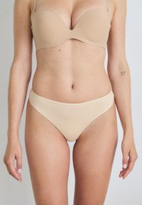 Beige gepolsterter BH mit Bügel, glattem Stoff und verstellbaren Trägern, kombiniert mit passenden nahtlosen Bikinihöschen, beide aus einem weichen, dehnbaren Material.