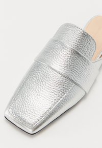 Metalliske sølv mules med en teksturert overflate, med en bred stropp over vamps og en spiss tåform. Glatt indre fôr.