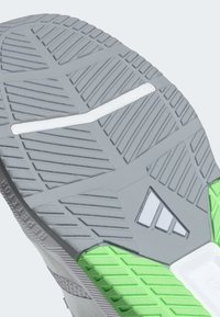 Gray rubber shoe sole with textured patterns, a white stripe, and green accents at the heel. Features a triangular logo detail.
