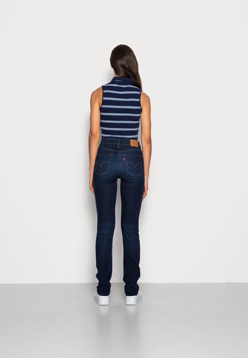 Haut sans manches rayé bleu marine et blanc associé à un jean skinny bleu foncé et des baskets blanches, vu de dos.