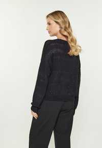 Maglione nero lavorato a maglia con vestibilità morbida, polsini e orlo a coste. Presenta un motivo testurizzato e un collo rotondo, indossato con pantaloni scuri.