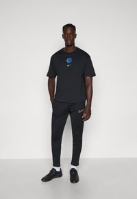 Sort Nike t-shirt med et lyseblåt logo; parret med sorte bukser og træningssko. Enkel, funktionel og moderne design.