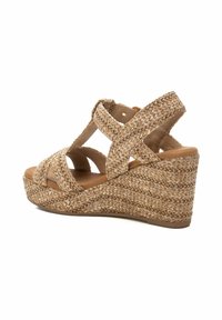 Sandalia cuña con material trenzado en tono marrón, que presenta correas entrecruzadas y una plantilla texturizada similar al yute. Diseño de punta redonda y plataforma.