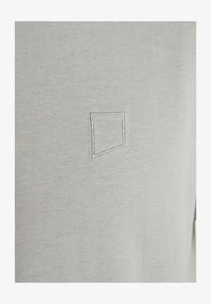 Světlé šedé látky s hladkou strukturou, která má prošívaný geometrický čtvercový detail v mírně tmavší šedé.