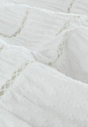 Tela blanca con rayas texturizadas y puntos en relieve. Los bordes presentan detalles de encaje, añadiendo dimensión al material.