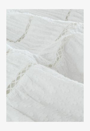 Tissu blanc avec des rayures texturées et des points en relief. Les bords présentent des accents de dentelle détaillés, ajoutant une dimension au matériau.