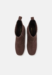 Botines de ante marrón con una textura suave, paneles laterales elásticos y tiradores para facilitar el calzado. Punta redondeada y diseño minimalista.