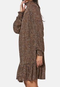 Braun gemustertes Kleid mit hohem Kragen, langen Ärmeln und gerafftem Saum. Hergestellt aus leichtem Stoff, mit einer strukturierten Oberfläche.