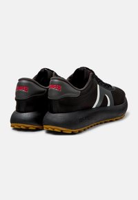 Black athletic shoes with a textured fabric upper, grey accents, a white design element, and a textured rubber sole with a yellow tread.