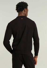 Felpa nera girocollo in cotone. Presenta polsini e orlo a coste, con una piccola etichetta con logo sul collo posteriore. Texture liscia.