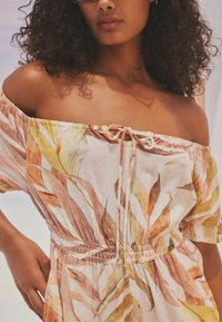 Robe décolletée en tissu léger, ornée d'un motif floral dans des nuances de rose, orange et vert, avec une taille élastique et des détails à cordon.