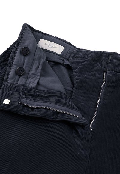 Donkerblauwe corduroy broek met een gestructureerd oppervlak, voorzien van een ritssluiting, dubbele knoopsluiting en een merketiket aan de binnenkant van de tailleband.